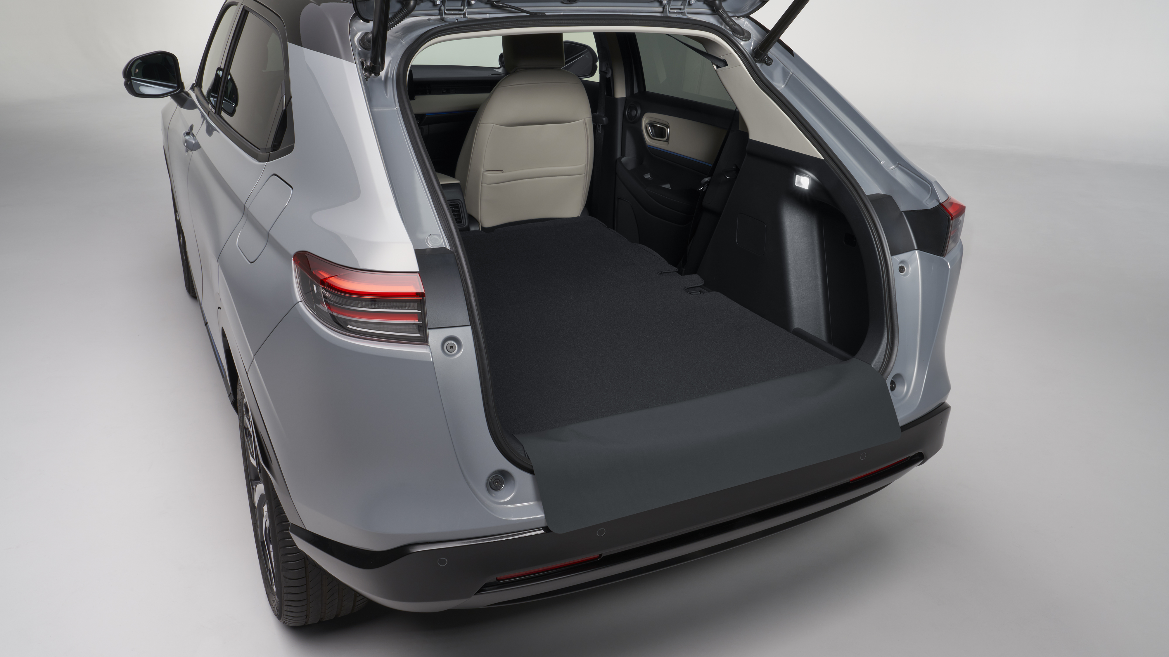Honda HR-V sedd bakifrån med öppen baklucka som visar det rymliga bagageutrymmet med nedfällda baksäten. Kupén har beige framsäten och ett plant, förlängt lastgolv i mörk klädsel.